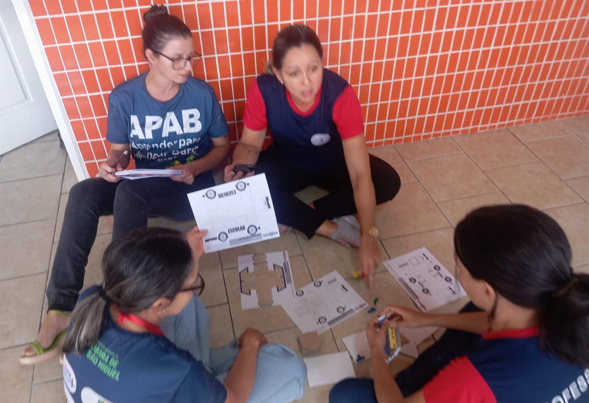 Professoras sentadas no chão trabalham em grupo com materiais impressos