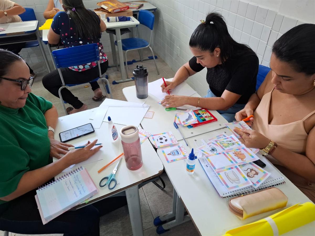 Professoras produzem material com lápis de cor, cola e fichas em uma oficina
